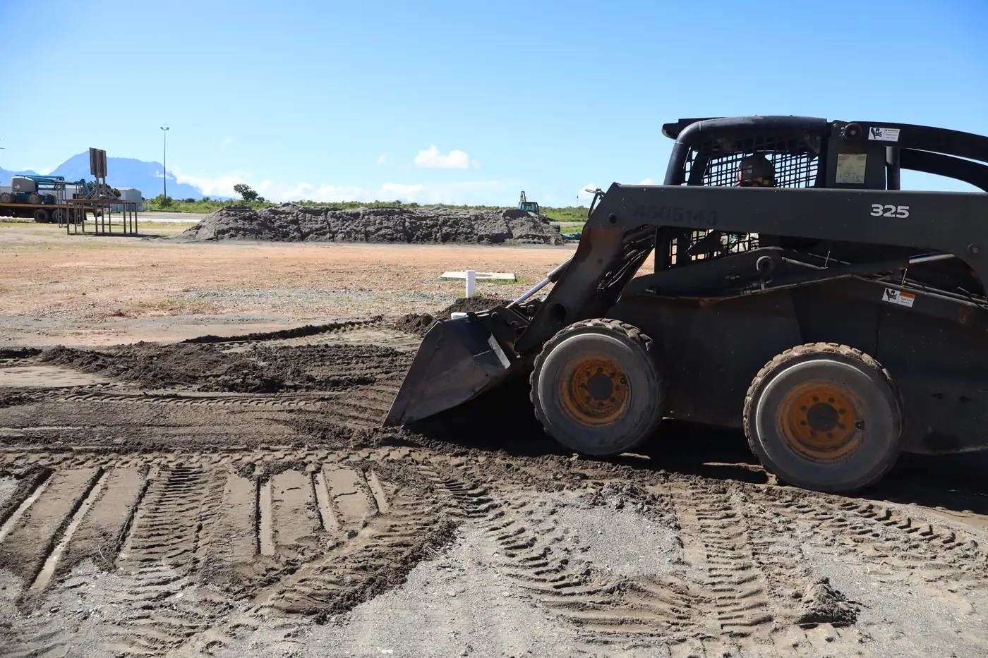Skid steer spreading and grading fill dirt across a work site